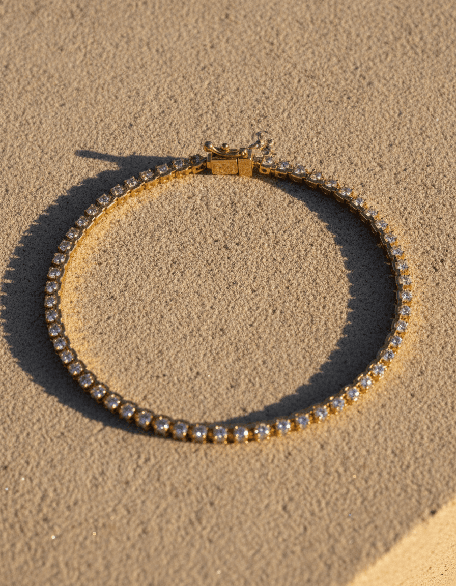 A lab-grown diamond line bracelet in 14K yellow gold with its box clasp, on warm sand