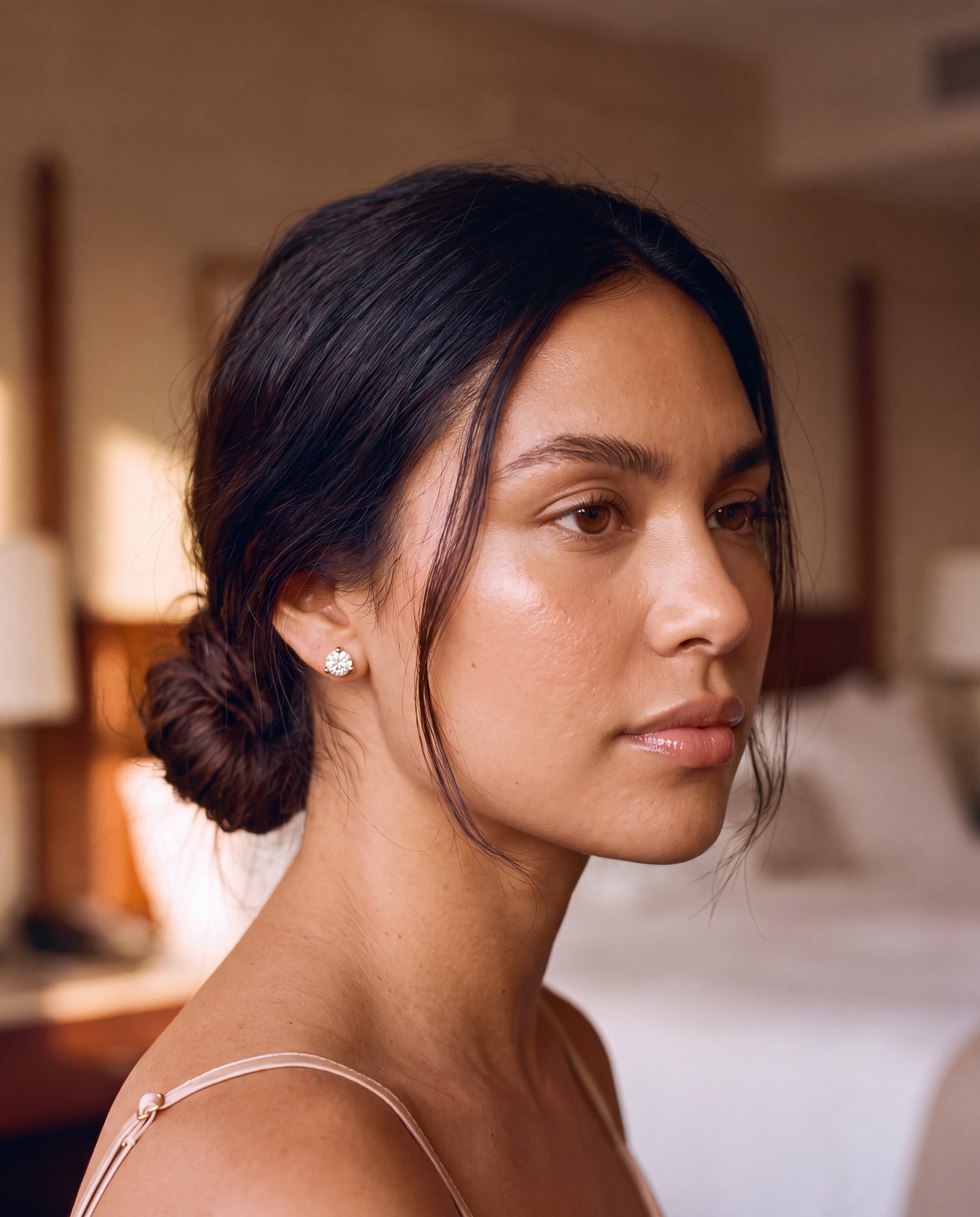 Profile of a sun-kissed young woman with a loose low bun in golden hotel light, wearing a round lab-grown diamond martini stud in 14K yellow gold